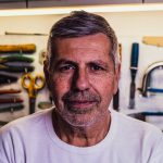 portrait photo of man in white crew neck t shirt with assorted hand tools in background